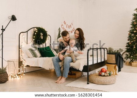 Happy parents play with baby on bed before Christmas