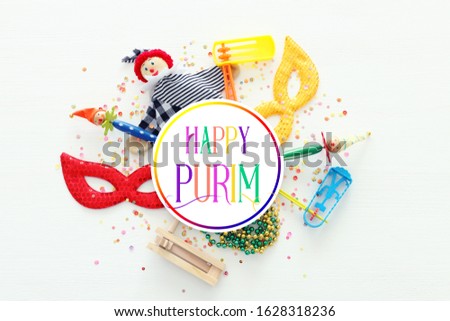 Party colorful noisemaker, mask and cute clown doll over white wooden background . Top view, flat lay