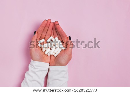 Woman's hand's holding a lot of white pills over pink background, top view