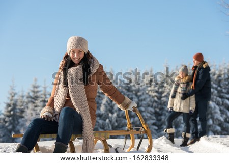 Young people enjoy sunny winter snow posing on wooden sledge