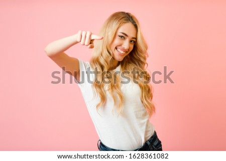 Hey, you! Excited woman pointing finger at camera and smiling over pink background