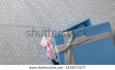 Wrapped gift box with white ribbon as a present for newly born child on white sheet background, top view, with copy space.Present for a colleague at work, family and friends