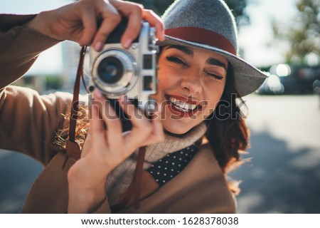 Portrait of happy fashionable woman holding vintage film camera laughing and looking at camera while walking at sunny city streets with vintage camera, Expressing positive emotions People Lifestyle