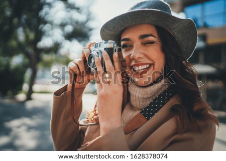 Young positive girl taking photo on vintage film camera while walking in the sunny city streets, happy female tourist in stylish outfit enjoying her trip in Europe, Vacation Tourism