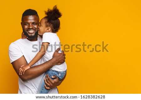 Preschool black girl kissing smiling father over yellow studio background, fatherhood concept, copy space Royalty-Free Stock Photo #1628382628