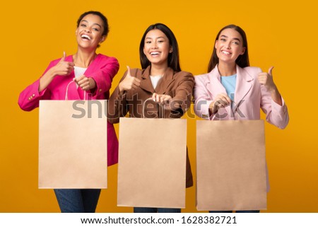 We Like Shopping. Three Girls Showing Blank Shopper Bags Gesturing Thumbs Up Posing In Studio On Yellow Background. Mockup