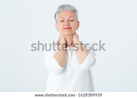 Adult happy woman folding her arms behind her head. Portrait of a mature woman with a short haircut and gray hair. Pain in the neck. Beautiful female on light background and copy space.