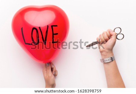 Rejection in love concept. Woman holding red heart balloon with love text and pinned with scissors over white background