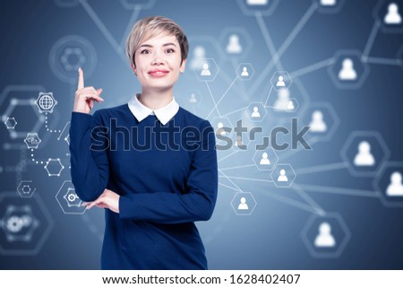 Smiling Asian businesswoman in blue dress standing over gray background with blurry social network interface. Concept of hiring