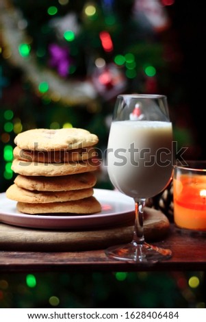 Cookies biscuits for Santa Claus near a christmas tree decorated with flashing lights,mistletoe and a glass of milk on a wooden tray, atmospheric Christmas picture