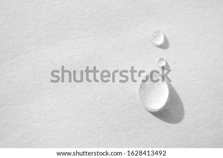 Water drop on white paper textured background with copy space and selective focus, close-up. Concept moisturizing macro, top view