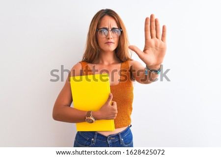Young beautiful redhead woman wearing glasses reading a book over isolated background with open hand doing stop sign with serious and confident expression, defense gesture