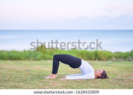 Young beautiful sportwoman practicing yoga. Coach teaching bridge pose at park