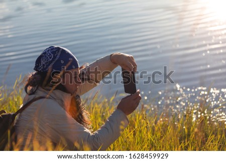 woman sits in grass and takes picture with cell phone