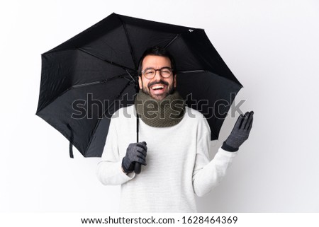 Caucasian handsome man with beard holding an umbrella over isolated white wall smiling a lot