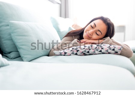 Happy asian girl lying on sofa with pillow at home