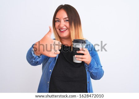 Young beautiful woman drinking take away glass of coffee over isolated white background happy with big smile doing ok sign, thumb up with fingers, excellent sign