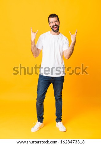 Full-length shot of man with beard over isolated yellow background making rock gesture