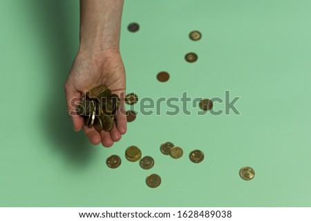 In the palm of a woman lies a handful of cash coins - the Israeli new shekel, agorot. Coins are still scattered under the palm. Light green background.