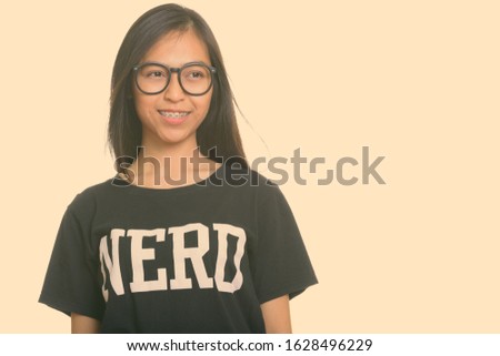 Studio shot of young happy Asian teenage nerd girl smiling while thinking