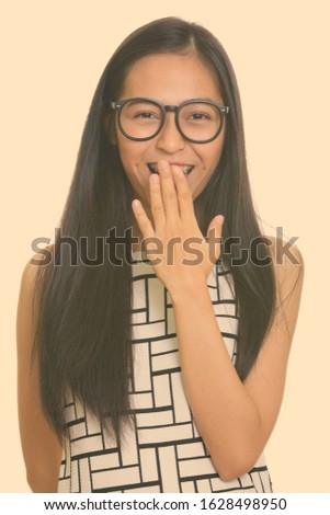Young happy Asian teenage nerd girl smiling and laughing while covering mouth