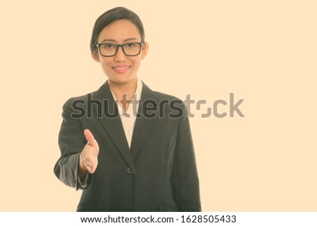 Studio shot of young happy Asian businesswoman smiling while giving handshake