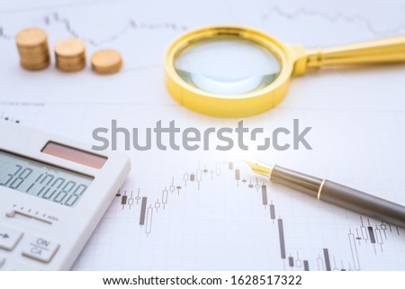 Calculator, magnifying glass, coins and pen on a bar chart-stock finance concept image