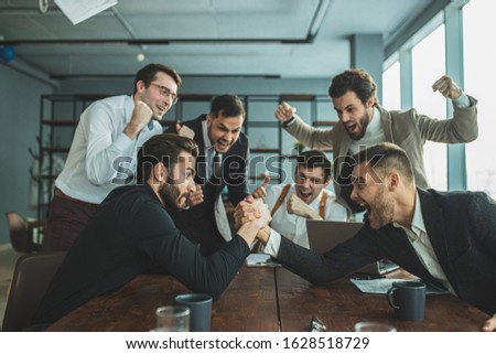 joyful coworking business men in tuxedo, cheerfully playing arm wrestling after working day in office