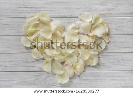 heart made of light rose petals on light wooden background