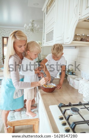 Yong mother with two sons cooking holiday pie in the kitchen. Casual lifestyle photo in real life interior