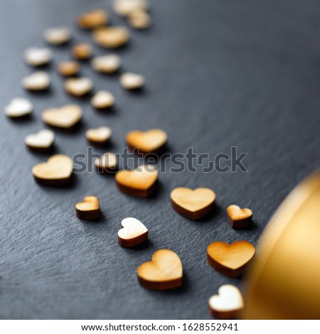 Love concept. Little wooden hearts falling out of a small gold gift box on a dark background. Side view with copy space
