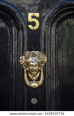 House number 5 on a black wooden front door with ornate door knocker in the form of a female head