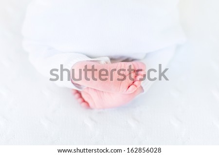 Close up picture of tiny baby feet on a white knitted blanket