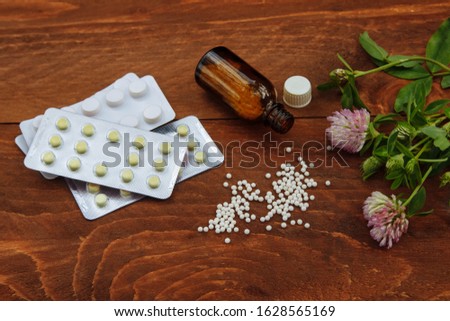  Pills scattered on the table from a glass bottle next to them are pills in a blister and a bunch of pink clover with flowers and green leaves a view from the top on a brown wooden background