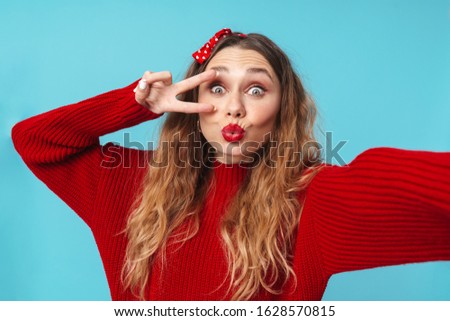 Image of amusing blonde woman gesturing peace sign and taking selfie photo isolated over blue background