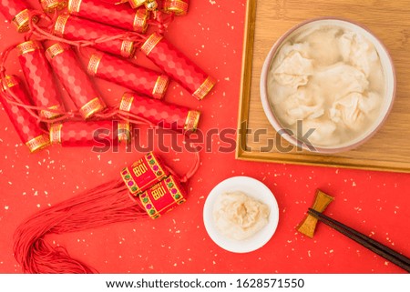 A bowl of shrimp wontons on red background for Chinese New Year with Chinese word in the picture means "good luck"