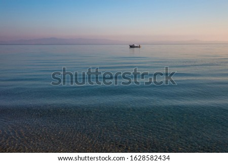 Early morning sea water landscape and silhouette of small boat at horizon. Quiet peaceful nature before sunrise. Horizontal color photography.