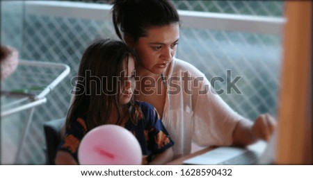 Mother teaching daughter a lesson in front of computer. Candid authentic parenting homework