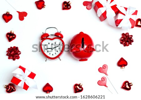 Alarm clock and piggy bank surrounded by gifts and hearts on white background. Saving money for St. Valentines Day. Top down composition. 