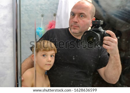 Surprised dad and son are photographed on a reflex camera in reflection in the mirror