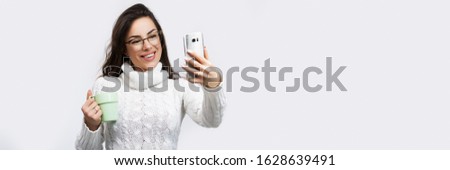 Portrait of a smiling casual beautiful woman using smartphone, taking selfie over white background. Banner crop for copy space