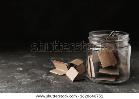 Glass jar with paper pieces on grey table, space for text