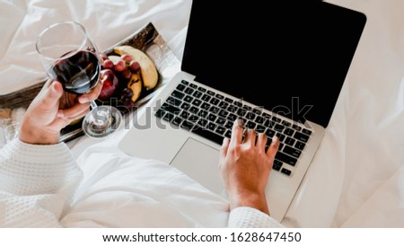 Picture of tourists businesswoman hands work with laptops, drink wine and eating fruits on a bed in the luxury hotel room, healthy food concept.