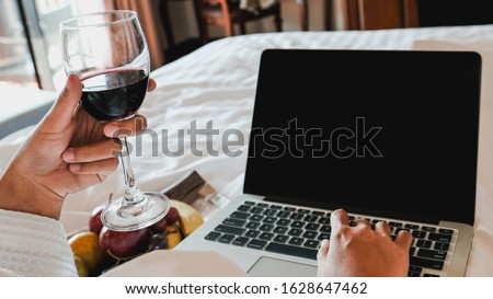 Picture of tourists businesswoman work with laptops, drink wine and eating fruits on a bed in the luxury hotel room, healthy food concept.