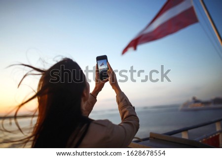 The girl tourist photographs a liner at sunset on the lake in Norway. Tourist takes sunset on the phone. Silhouette at sunset of young woman.Travelling, lifestyle, adventure, wild nature concept.