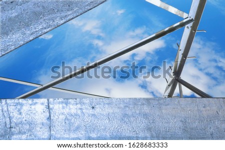 Metallic, steel structure in silver gray tones against a blue sky with clouds. Abstract background with metal architecture details.