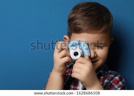 Little photographer taking picture with toy camera on blue background