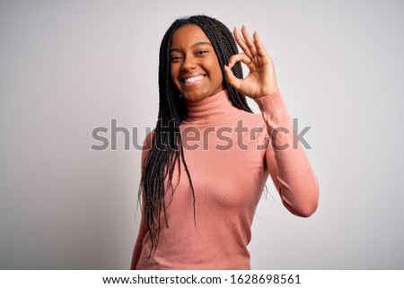 Young african american woman standing casual and cool over white isolated background smiling positive doing ok sign with hand and fingers. Successful expression.