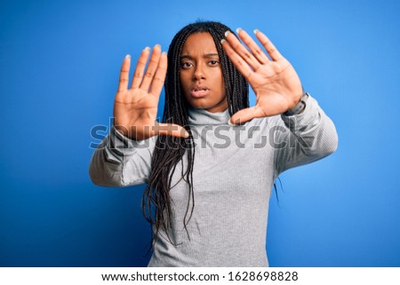 Young african american woman standing wearing casual turtleneck over blue isolated background doing frame using hands palms and fingers, camera perspective