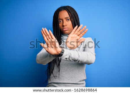 Young african american woman standing wearing casual turtleneck over blue isolated background Rejection expression crossing arms doing negative sign, angry face